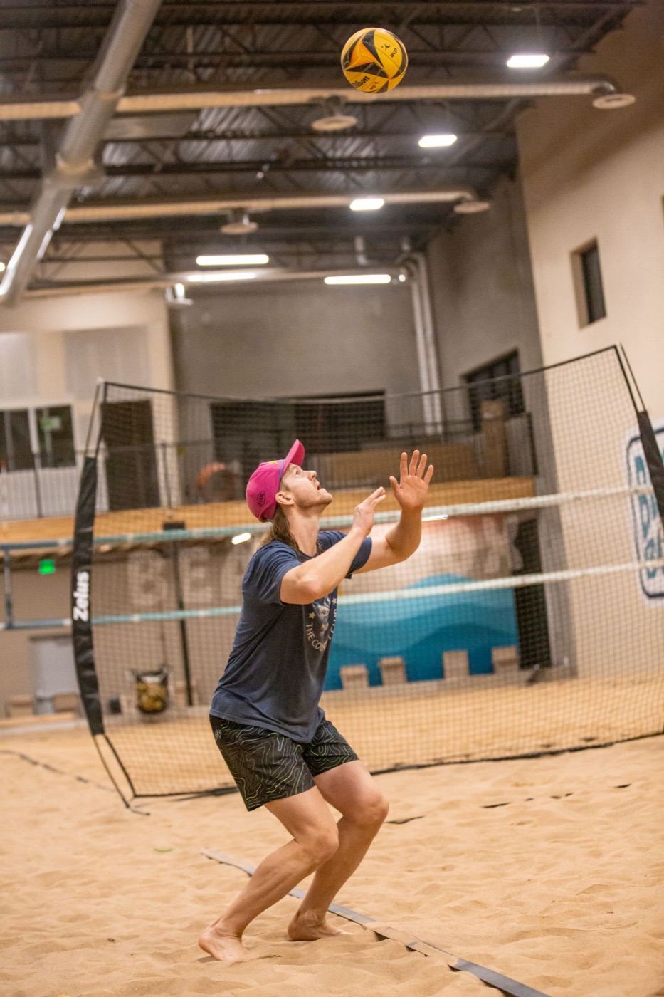 Player in a pink cap setting the ball on an indoor sand court